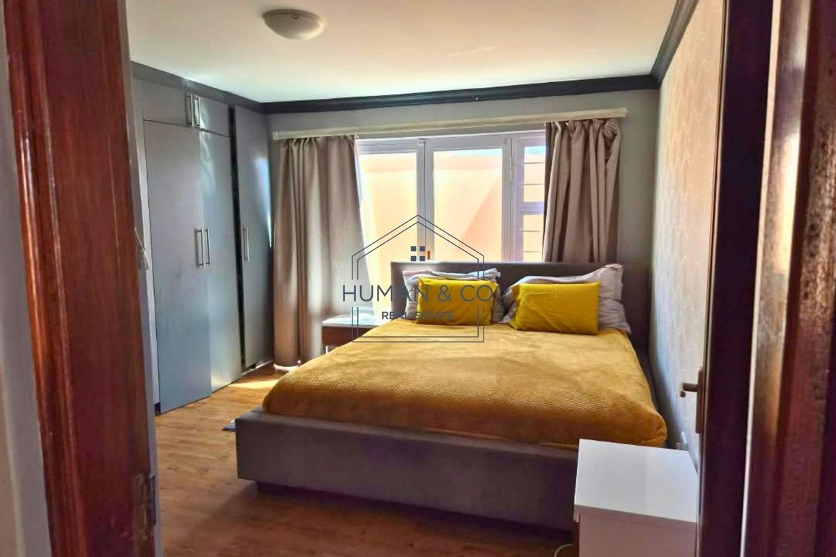 A bedroom featuring laminate flooring, built-in cupboards, and a window with curtains.