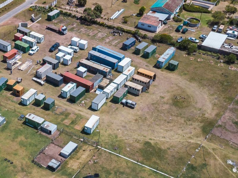 Aerial view of a large vacant residential plot featuring multiple shipping containers and perimeter fencing.