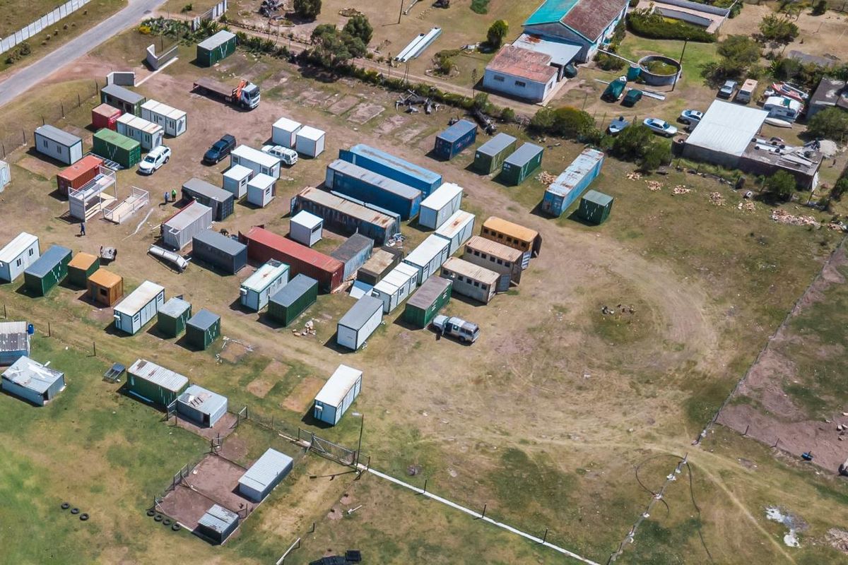 Aerial view of a large vacant residential plot featuring multiple shipping containers and perimeter fencing.