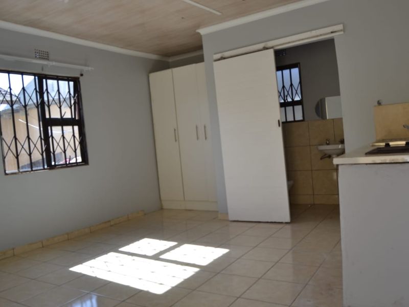 An open-plan living area featuring tiled floors, built-in cupboards, and a compact kitchen space with a hob and sink.