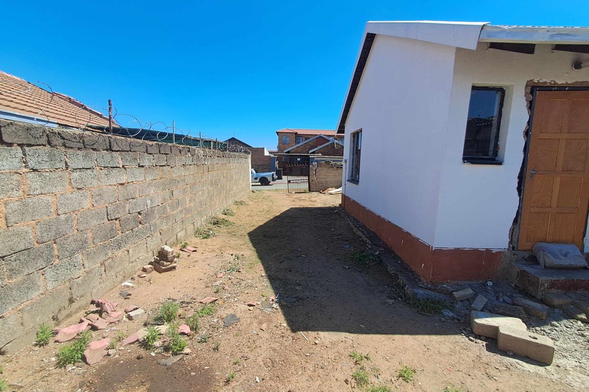 Rear exterior view of the property featuring a perimeter brick wall with razor wire and an unfinished entrance area requiring repair.