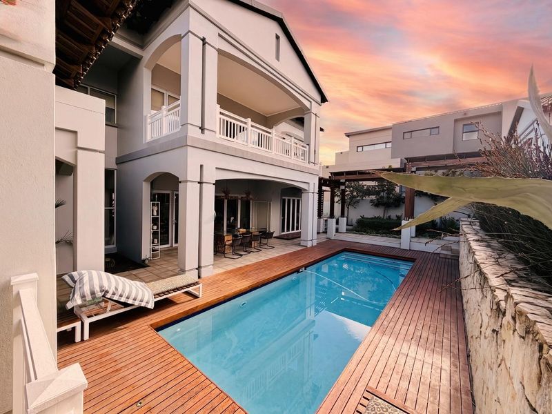 A well-maintained rear exterior featuring a swimming pool with timber decking, a covered patio area, and a multi-level residential facade.
