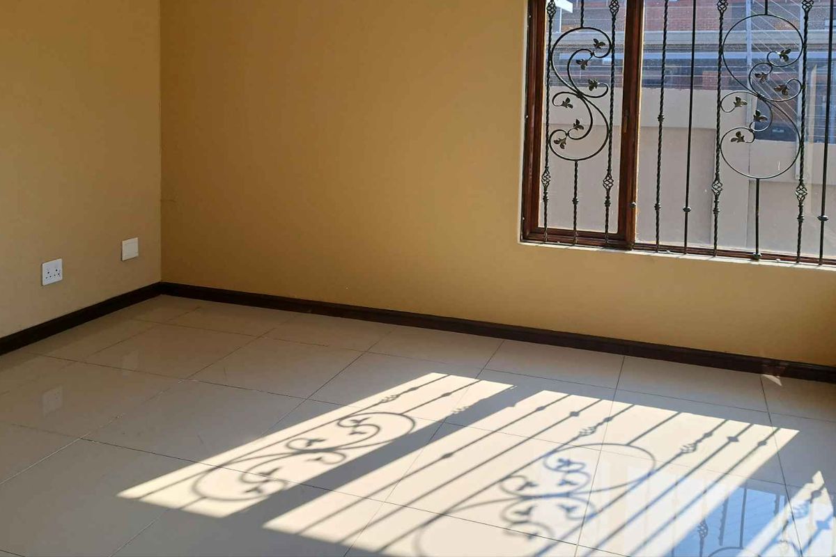An empty bedroom featuring tiled flooring, neutral wall paint, and security bars on the window.