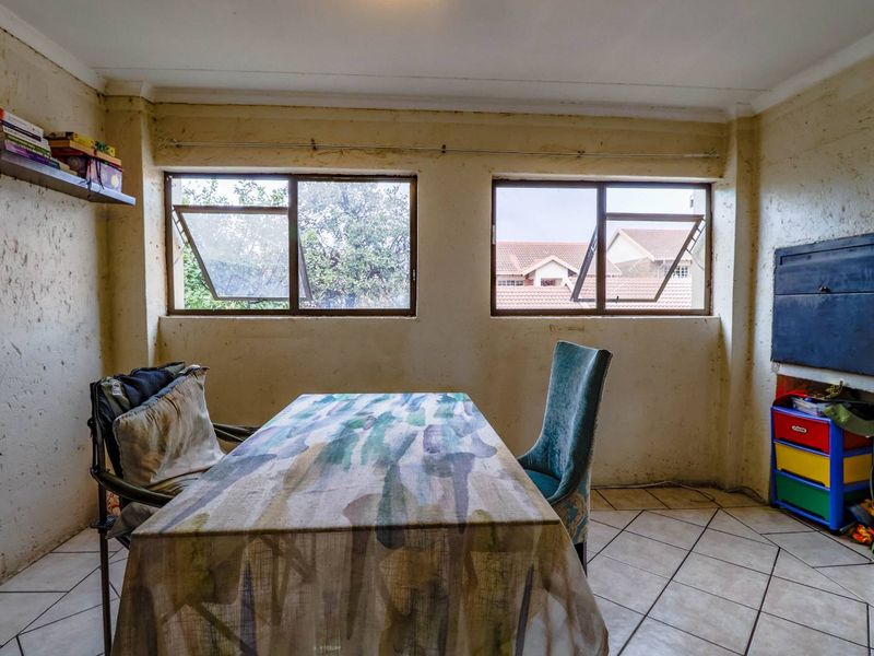 A dining area featuring tiled flooring and aluminium windows, currently requiring significant wall repairs and cosmetic refurbishment to improve the overall condition.