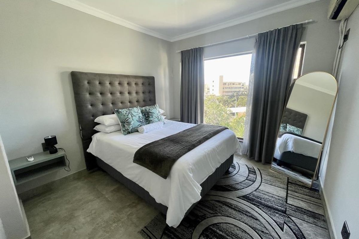 A well-maintained bedroom featuring tiled flooring, a wall-mounted bedside shelf, and an integrated air conditioning unit with large window access.