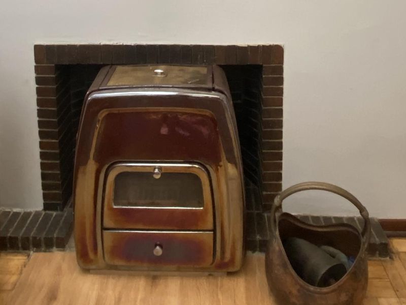 A living room featuring a vintage freestanding wood-burning stove set within a brick fireplace surround and finished with parquet flooring.