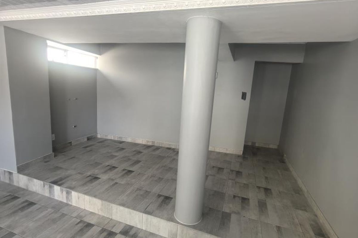 An open-plan interior space featuring a raised platform area, a central structural column, and modern grey tiled flooring throughout.