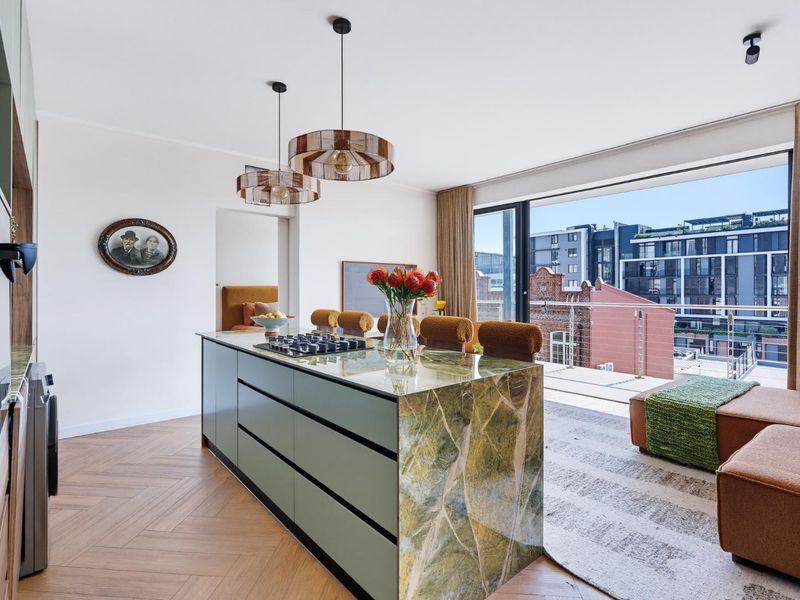 Modern open-plan kitchen featuring a stone-topped island with integrated gas cooktop, herringbone timber flooring, and seamless access to a private balcony.