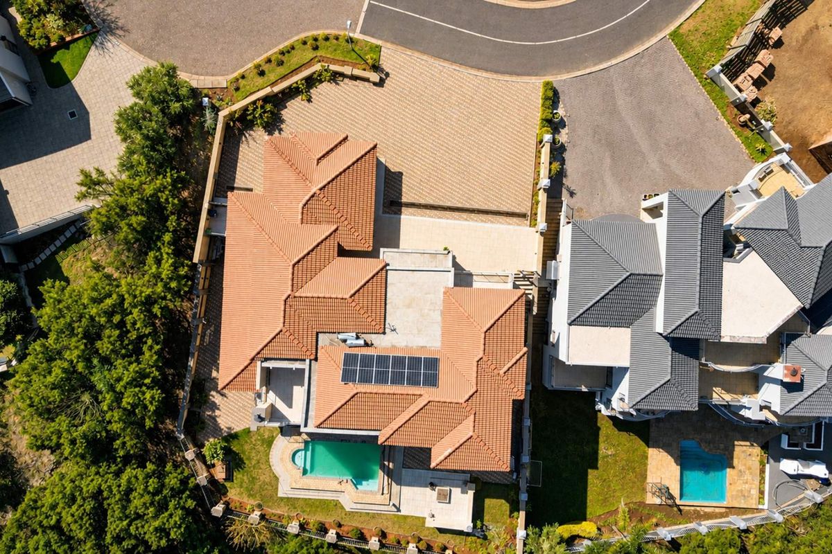 Aerial view of the property showcasing the tiled roof, integrated solar panels, private swimming pool, and paved driveway area.