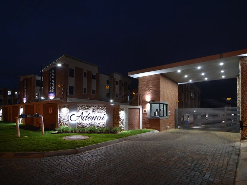 Night view of the secure entrance to Adonai townhouse complex, featuring brick and stone architecture, automated gate, and guard house.