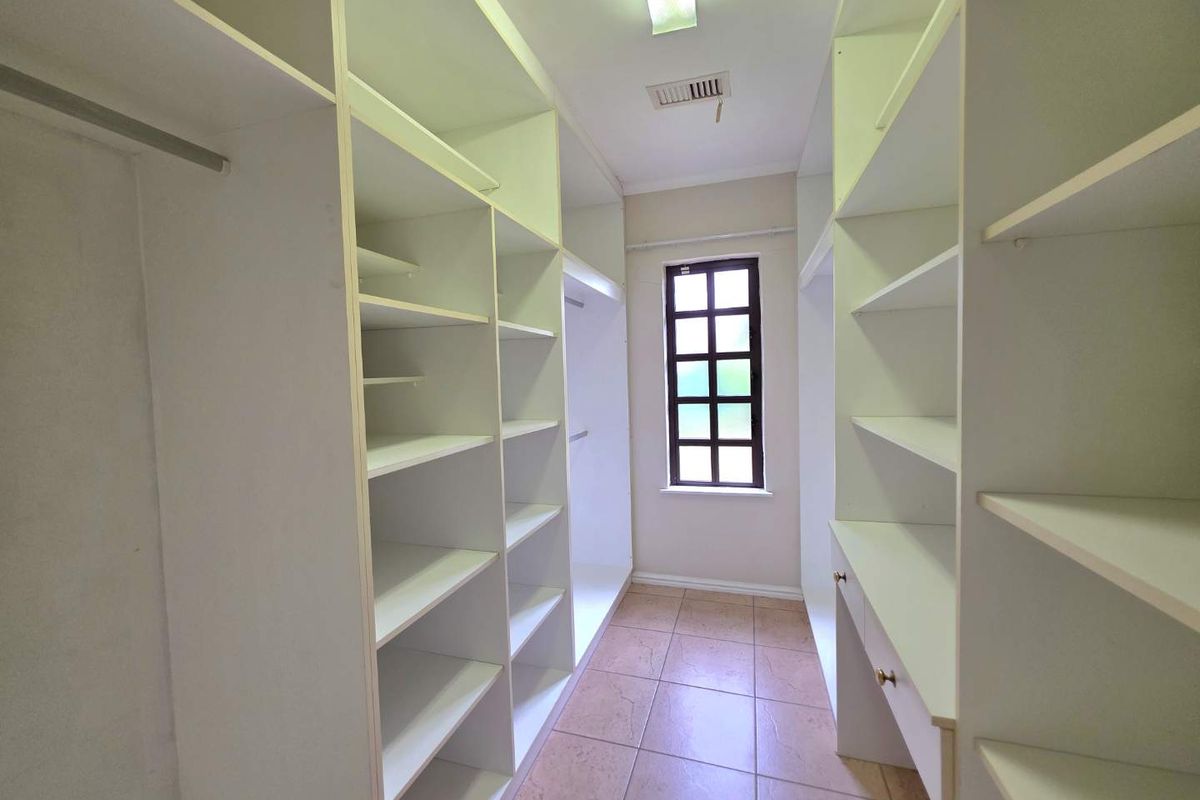 A walk-in closet or dressing room featuring extensive built-in white cabinetry, tiled flooring, and a window providing natural light.