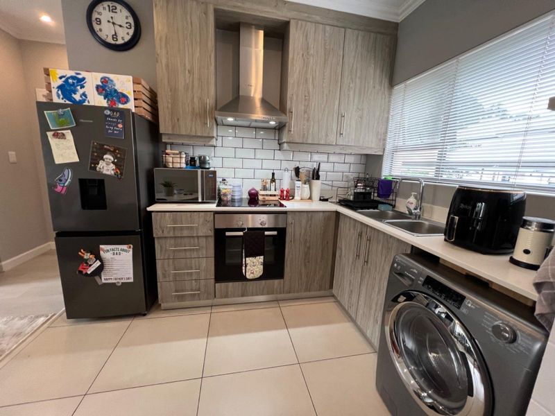 A modern kitchen featuring wood-grain cabinetry, subway tile backsplash, stainless steel appliances, and tiled flooring, offering a functional and contemporary cooking space.