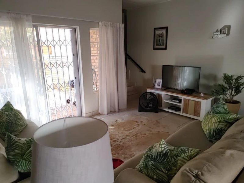 A comfortable living room featuring tiled flooring, a sliding glass door with security gate, and direct access to the staircase.