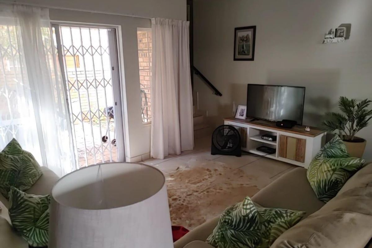 A comfortable living room featuring tiled flooring, a sliding glass door with security gate, and direct access to the staircase.