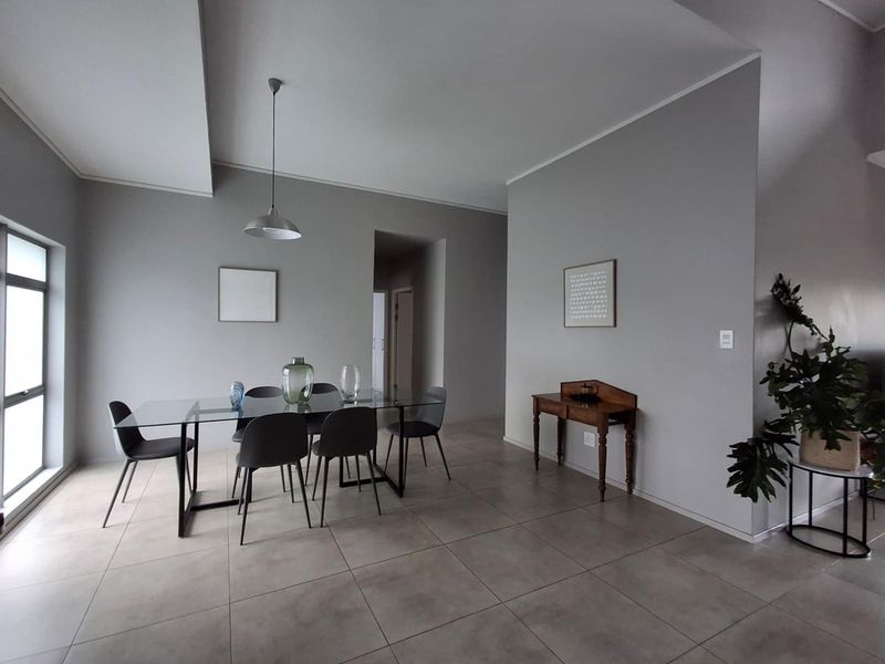 A bright and spacious dining area featuring neutral grey walls, large format floor tiles, and a modern pendant light fixture.