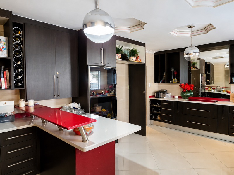 Modern kitchen featuring dark wood cabinetry, contrasting red accents, stone countertops, integrated wine storage, and high-quality tiled flooring.