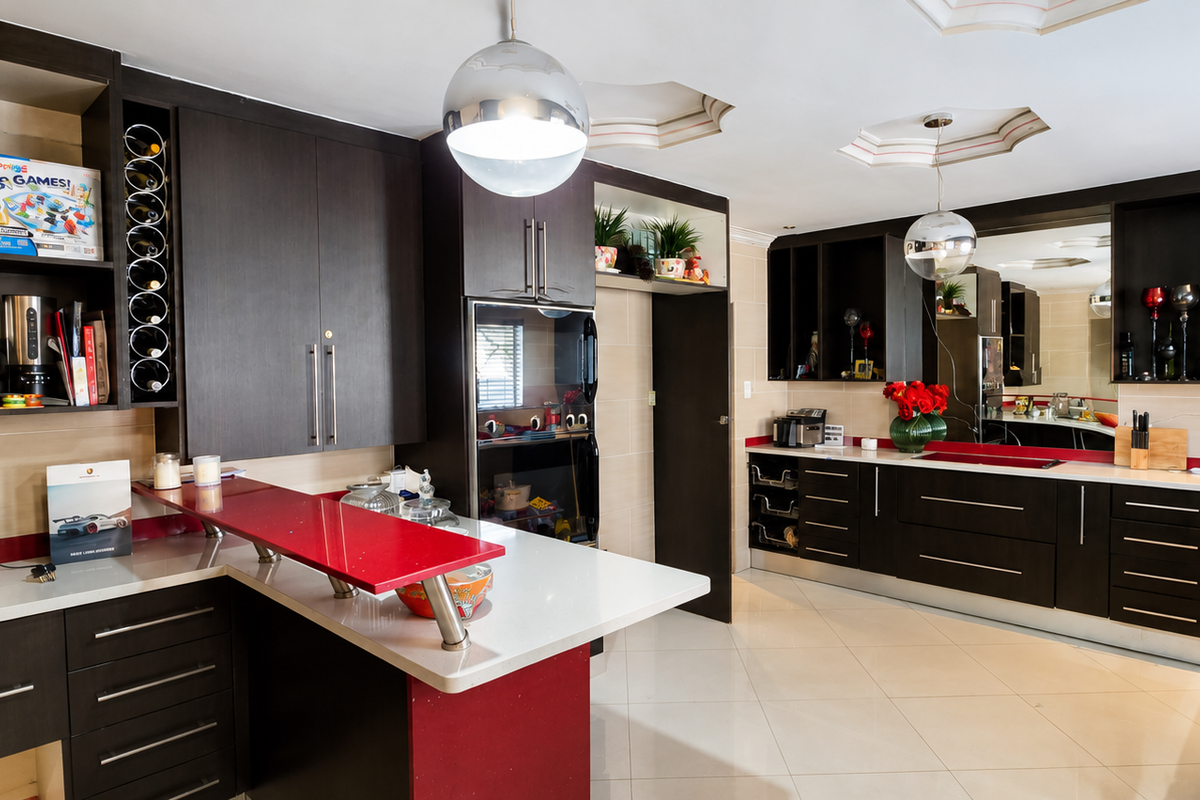 Modern kitchen featuring dark wood cabinetry, contrasting red accents, stone countertops, integrated wine storage, and high-quality tiled flooring.