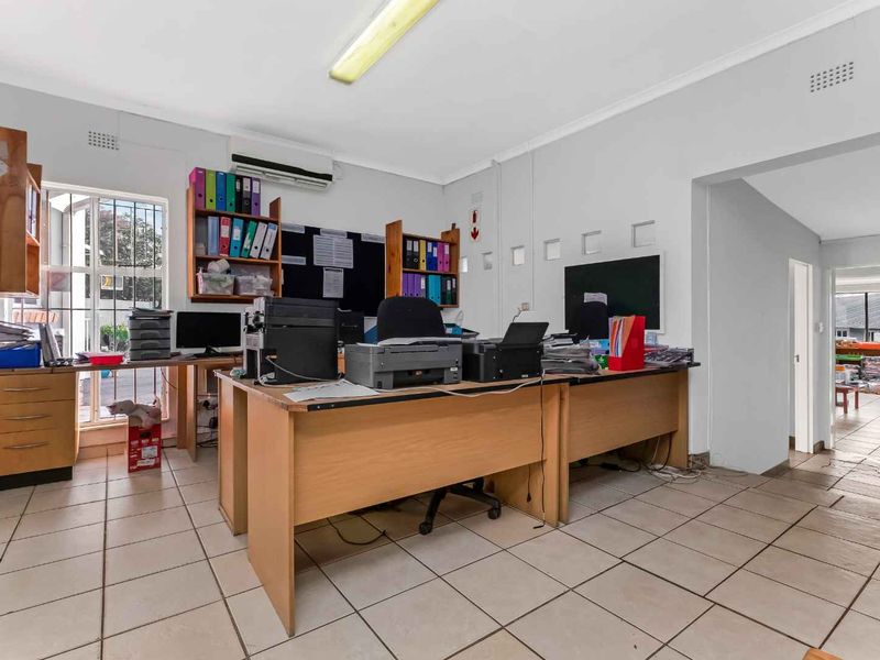 Functional office space featuring ceramic floor tiles, air conditioning, and secure window bars, offering a practical workspace environment.