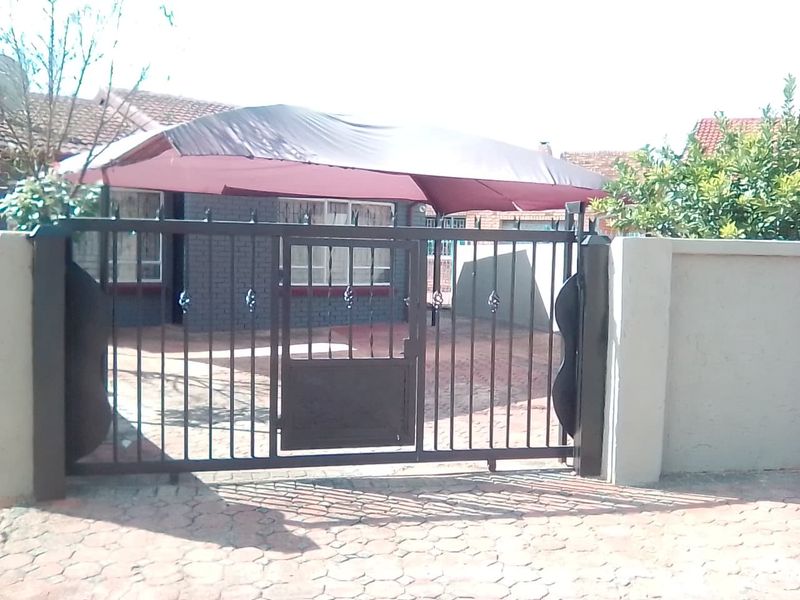 Front view of the property featuring a metal security gate, paved driveway, and a shade sail covering the entrance area.