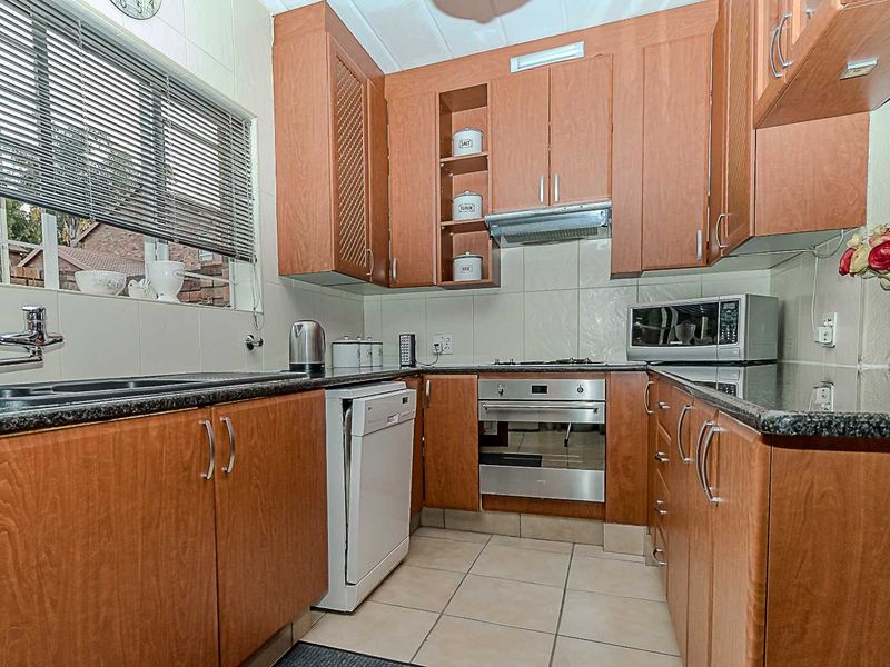 A functional kitchen featuring wood-finish cabinetry, granite countertops, built-in oven, gas hob, and tiled flooring with a neutral backsplash.