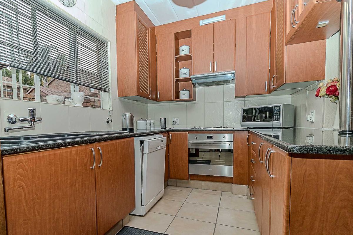A functional kitchen featuring wood-finish cabinetry, granite countertops, built-in oven, gas hob, and tiled flooring with a neutral backsplash.