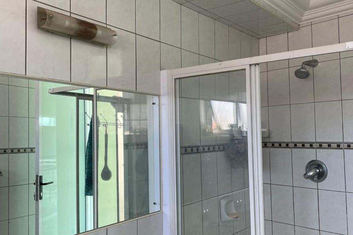 A functional bathroom featuring a shower enclosure, granite-topped vanity with basin, wall-mounted mirror, and tiled wall finishes.