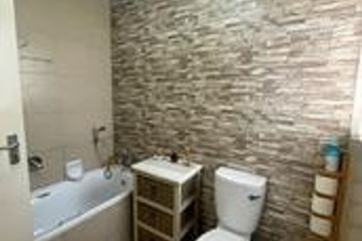 A functional bathroom featuring a bathtub, toilet, bidet, and a decorative stone-cladding feature wall.