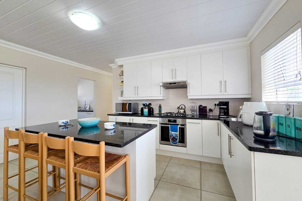 Modern kitchen featuring white cabinetry, contrasting black granite countertops, a central island with breakfast bar seating, and integrated stainless steel appliances.