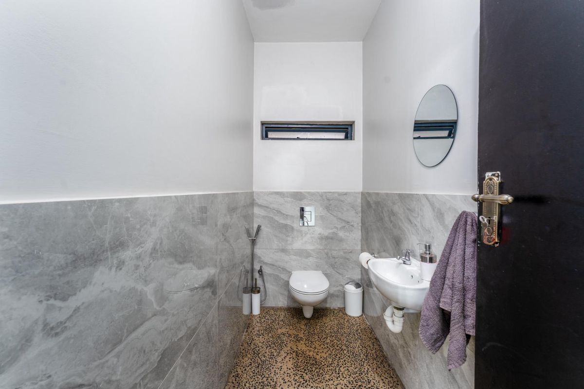 A modern guest bathroom featuring grey marble-effect wall tiles, a wall-mounted toilet, and a compact basin with a sleek finish.