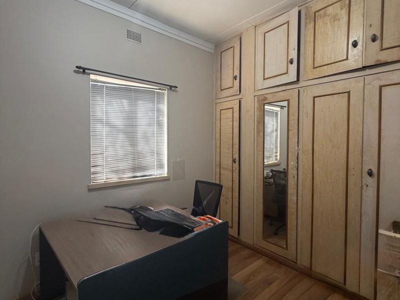 A functional office space featuring extensive built-in cabinetry with integrated mirror and durable laminate flooring, providing ample storage and a dedicated workspace.