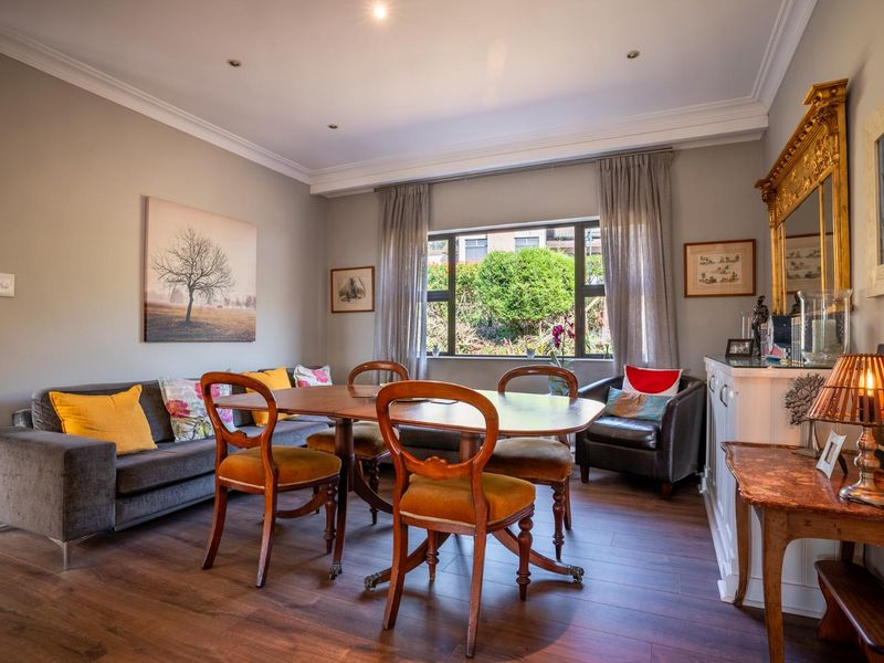 A well-maintained dining room featuring laminate flooring, crown molding, and recessed lighting, with a large window providing natural light and garden views.
