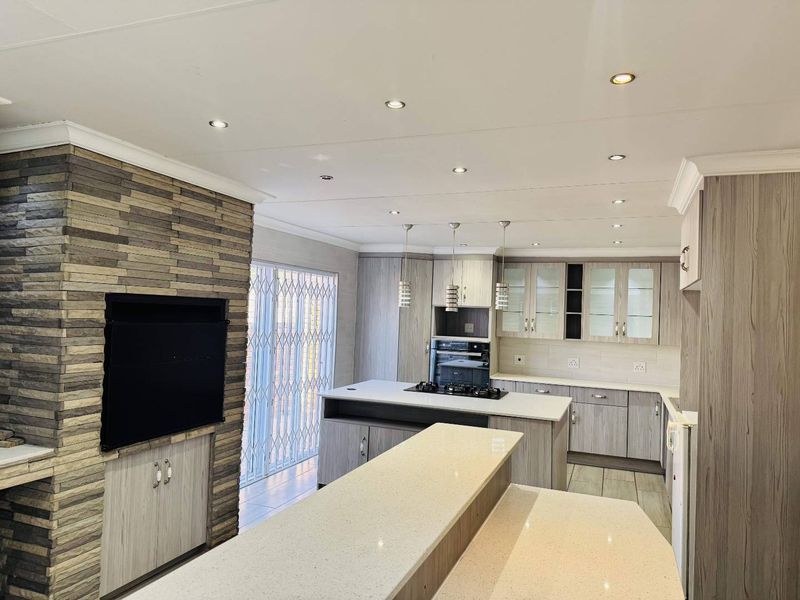 Modern open-plan kitchen and living area featuring a stone-clad feature wall with built-in braai, quartz countertops, and sleek laminate cabinetry.