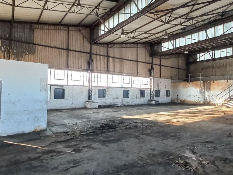 Spacious industrial warehouse featuring high ceilings, exposed steel trusses, clerestory windows, and a mezzanine staircase, offering a versatile open-plan workspace.