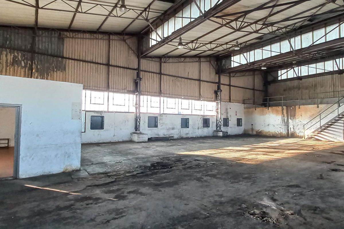 Spacious industrial warehouse featuring high ceilings, exposed steel trusses, clerestory windows, and a mezzanine staircase, offering a versatile open-plan workspace.