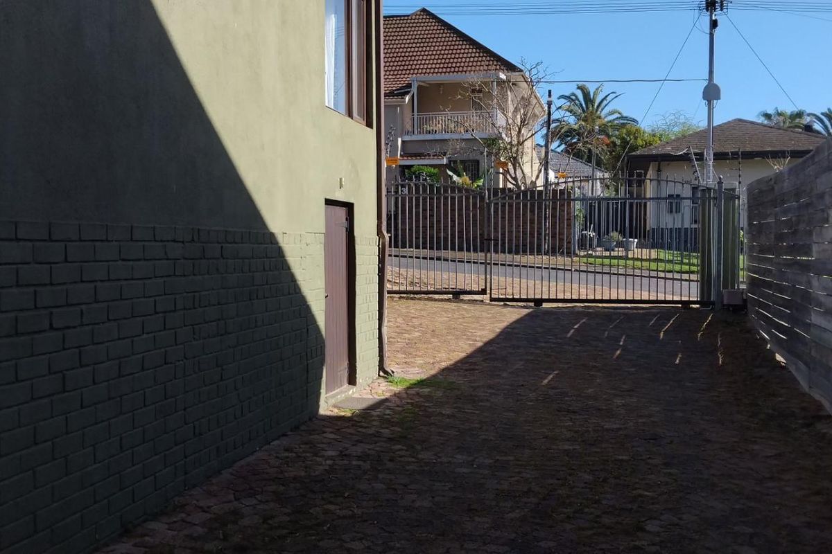 A view of the side exterior area of the apartment building, featuring paved ground, a metal security gate, and perimeter fencing.
