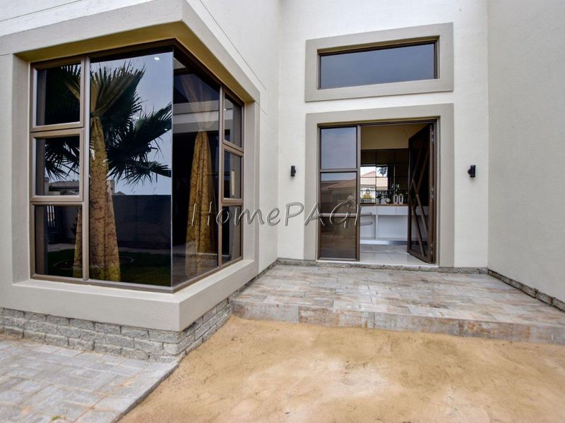 Rear exterior view featuring a tiled patio, modern aluminium-framed windows, and a glass entrance door leading into the home.