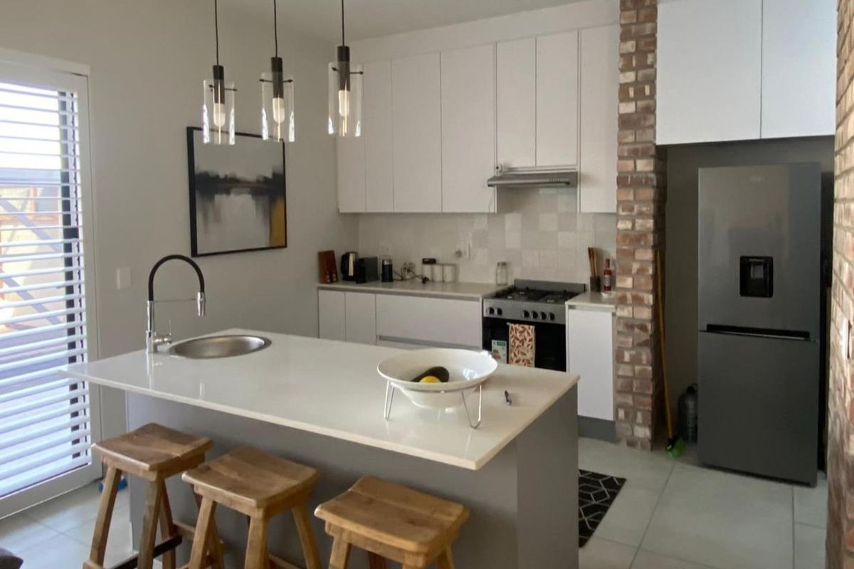 Modern kitchen featuring a central island with quartz countertops, built-in cabinetry, gas stove, and a distinctive exposed brick pillar accent.