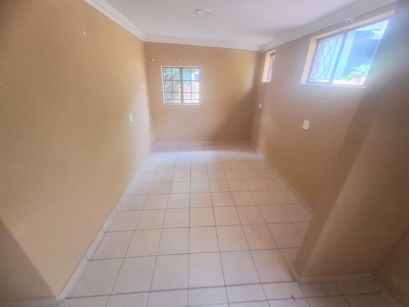 An empty bedroom featuring tiled flooring, security bars on the windows, and neutral wall paint, offering a blank canvas for personalization.