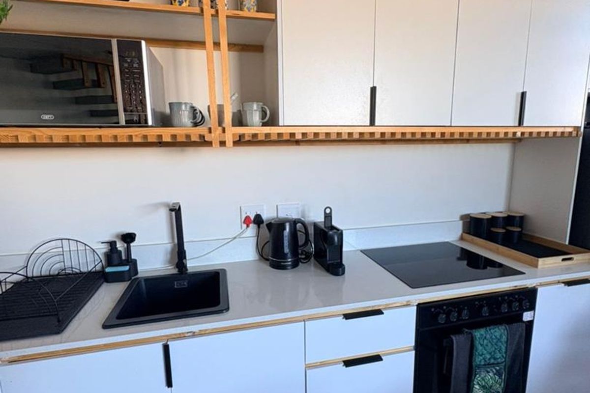 Modern kitchen featuring white cabinetry with wood trim, integrated oven, induction hob, and a sleek black sink with matching faucet.