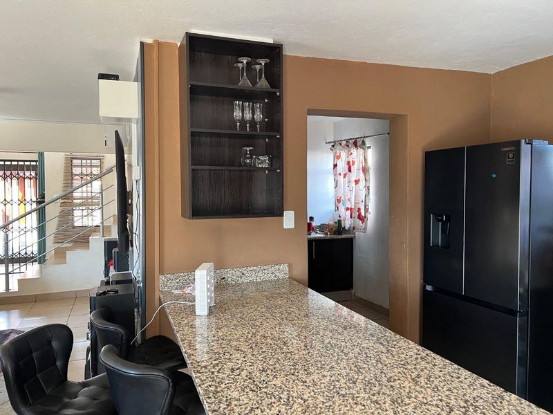 Open plan living area featuring a granite breakfast bar, built-in shelving, and access to a secondary kitchen or scullery area.
