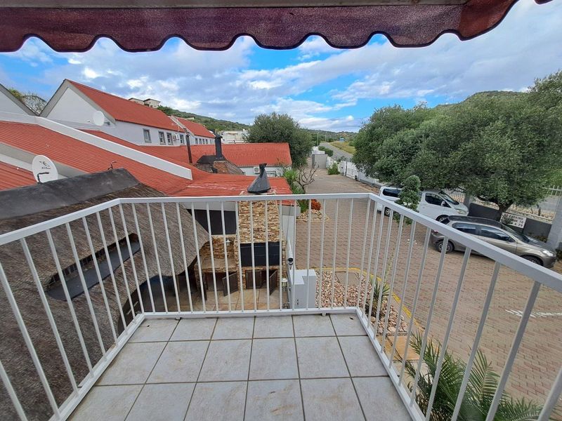 A private balcony featuring tiled flooring, a white metal balustrade, and a retractable awning, overlooking the complex grounds and parking area.