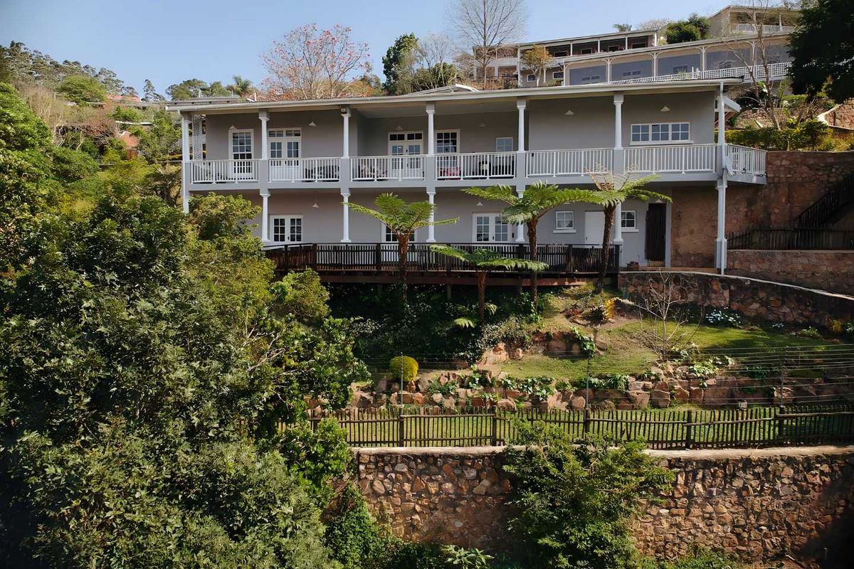 Rear view of a double-story townhouse featuring extensive timber decking, white balustrades, and tiered stone retaining walls set within a landscaped garden.