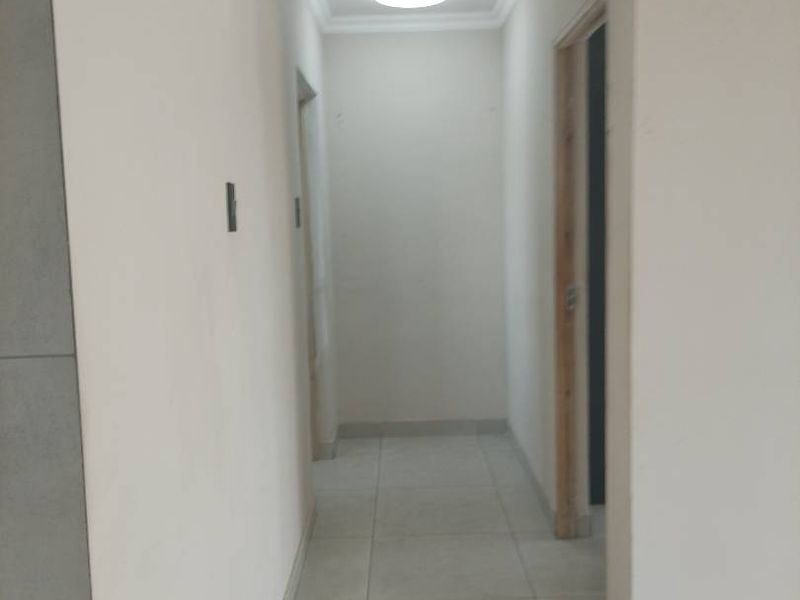 A clean, empty hallway featuring neutral tiled flooring and a recessed ceiling light, providing access to adjacent rooms.