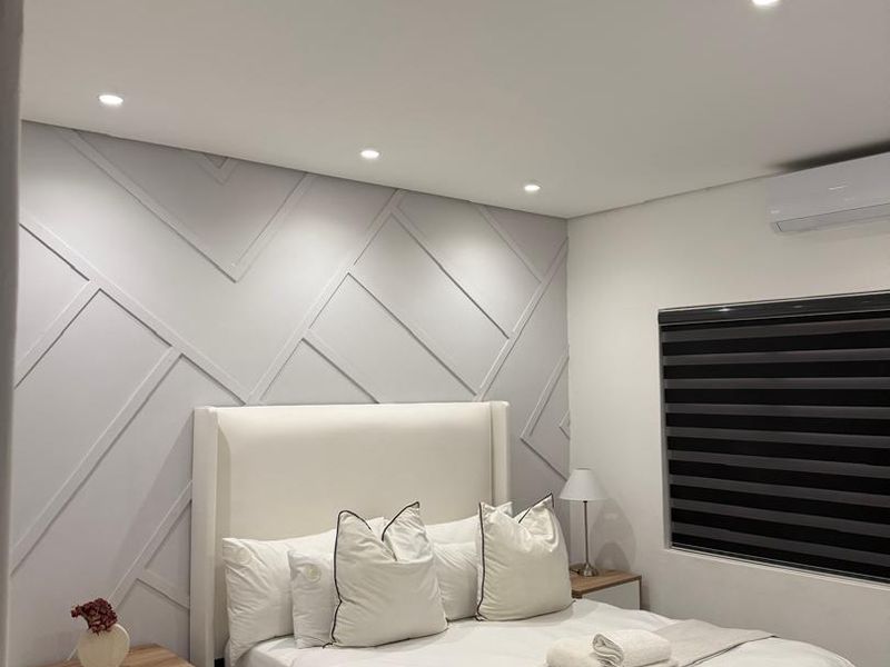 Modern bedroom featuring decorative wall paneling, recessed downlighting, split-system air conditioning, and sleek tiled flooring.