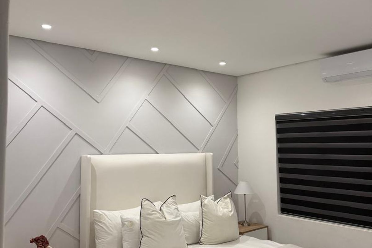 Modern bedroom featuring decorative wall paneling, recessed downlighting, split-system air conditioning, and sleek tiled flooring.