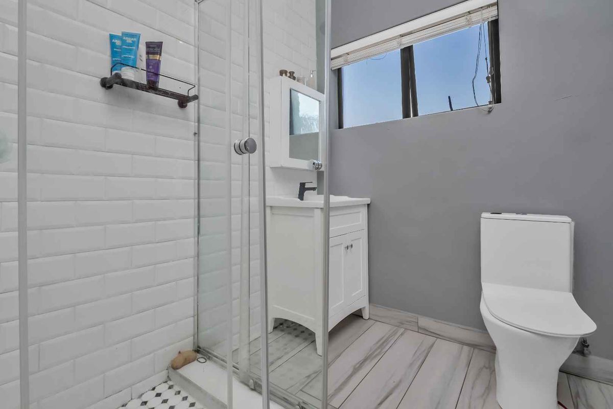 A compact bathroom featuring a glass-enclosed shower, a white vanity cabinet with a basin, and a modern toilet, finished with subway wall tiles.