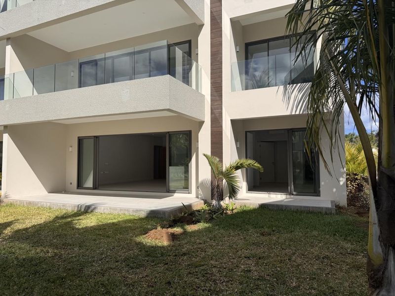 Rear view of a modern apartment building featuring ground floor patios with sliding glass doors and upper level balconies with glass balustrades.