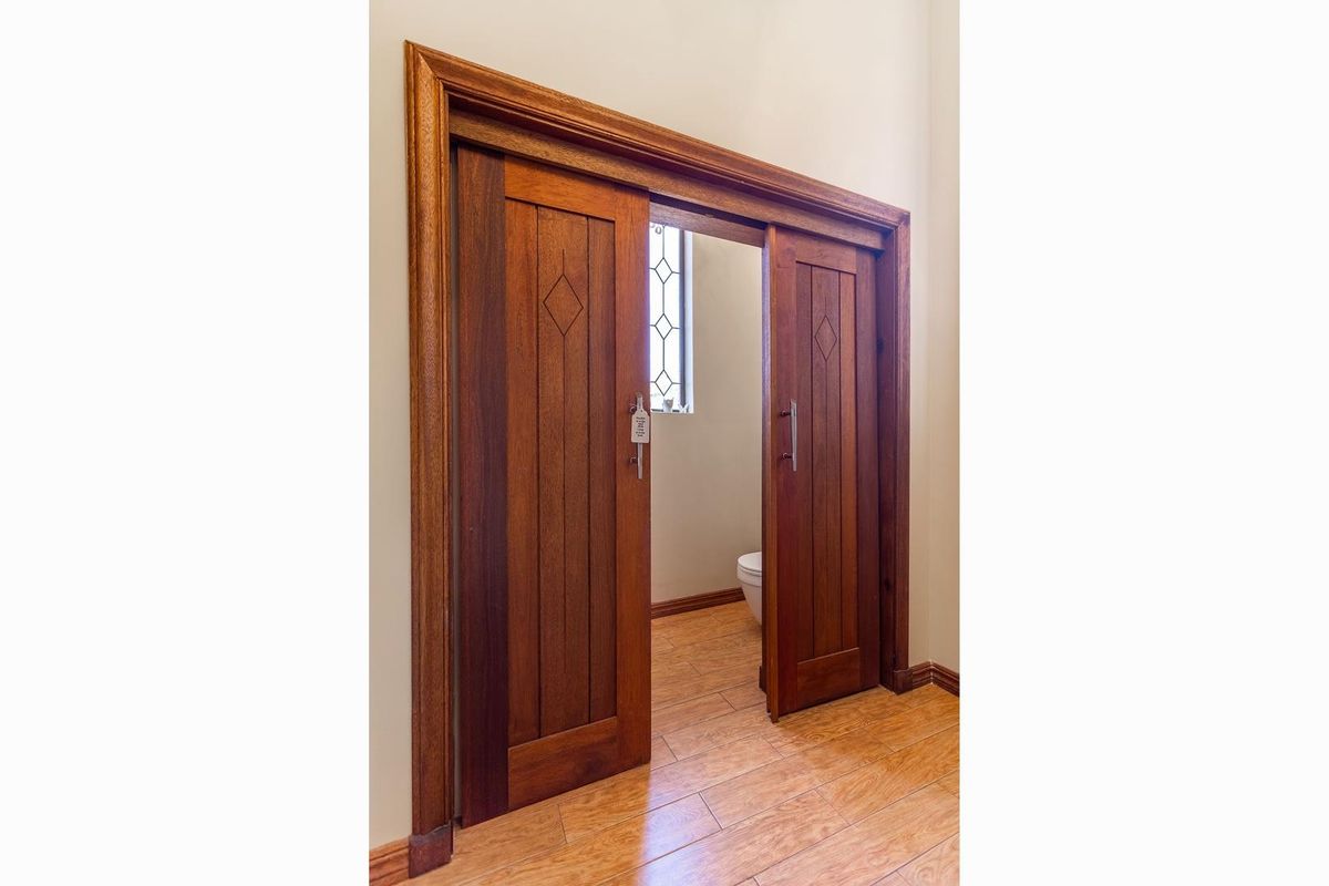 A view into a bathroom featuring custom timber sliding doors with decorative paneling and wood-look tile flooring.