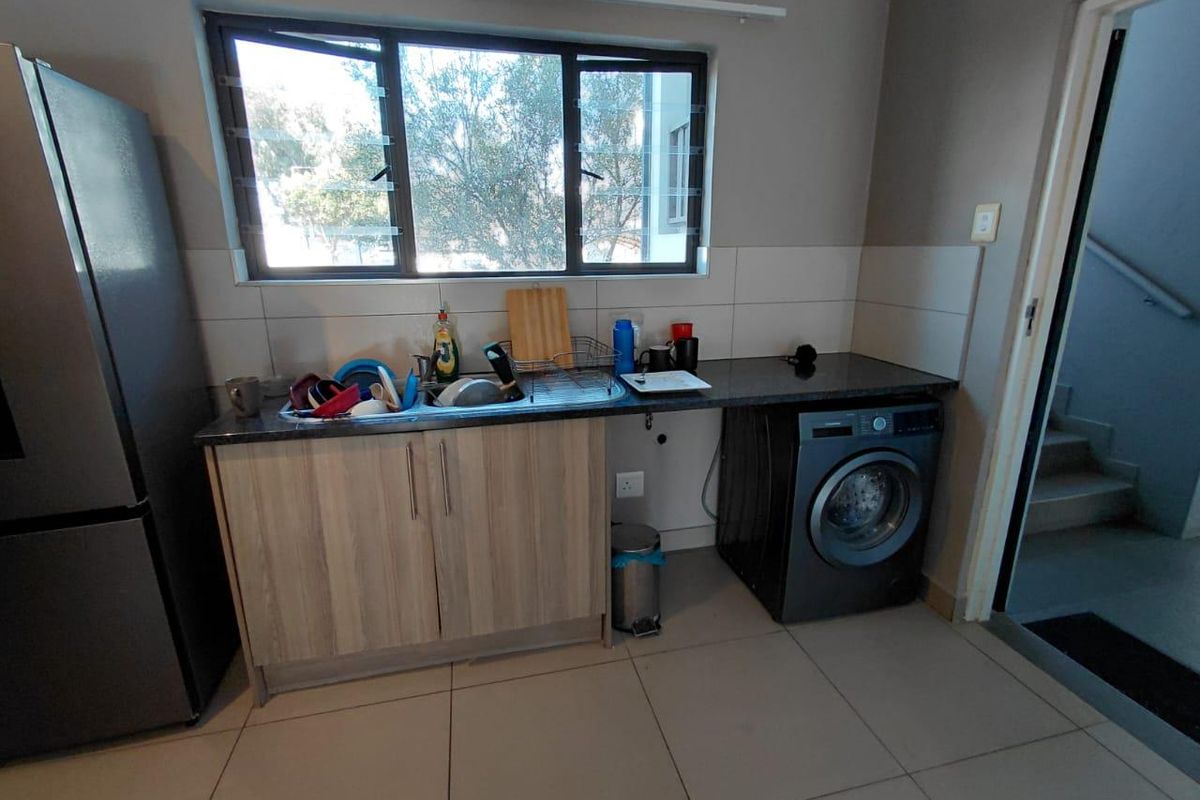 A functional kitchen area featuring granite countertops, a stainless steel sink, tiled splashbacks, and space for a washing machine.