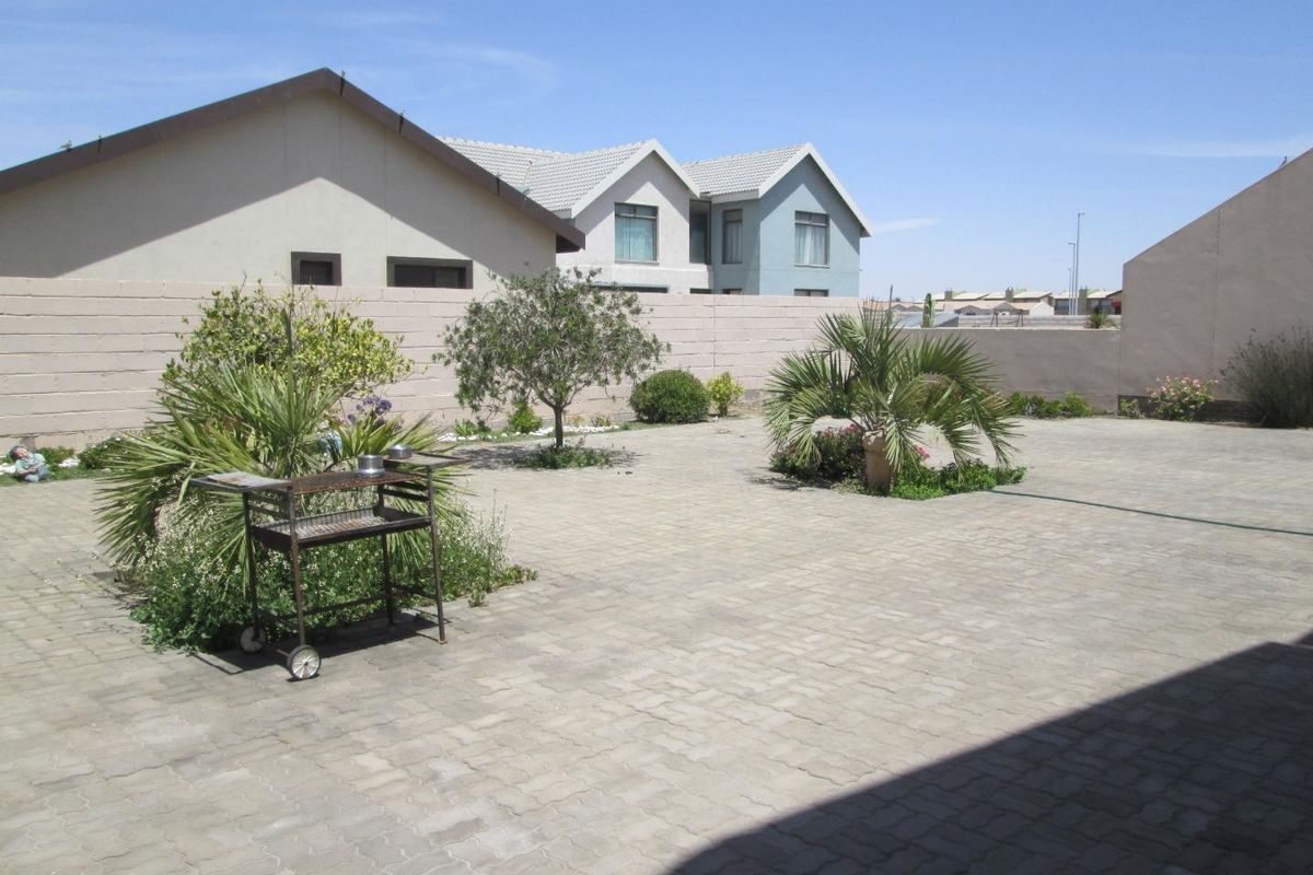 A spacious, paved rear courtyard featuring established garden beds and perimeter boundary walls, offering a low-maintenance outdoor area.